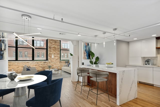 kitchen featuring a center island, white cabinets, hanging light fixtures, light hardwood / wood-style floors, and brick wall