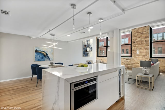 kitchen featuring white cabinets, oven, hanging light fixtures, a kitchen island, and brick wall