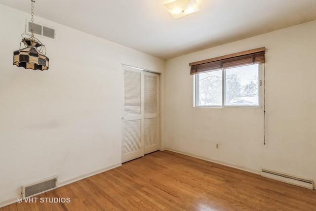 unfurnished bedroom with light hardwood / wood-style floors, baseboard heating, and a closet