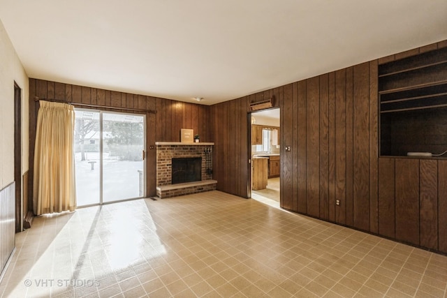 unfurnished living room featuring wooden walls and a brick fireplace