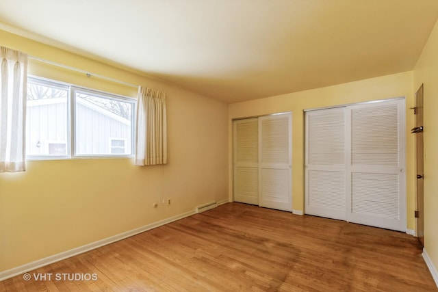 unfurnished bedroom featuring hardwood / wood-style floors, a baseboard heating unit, and multiple closets