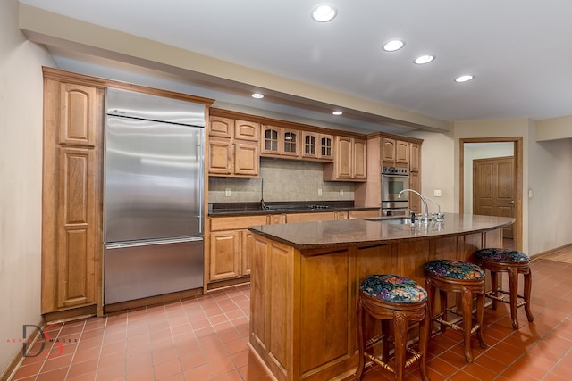 kitchen featuring sink, an island with sink, decorative backsplash, light tile patterned flooring, and appliances with stainless steel finishes