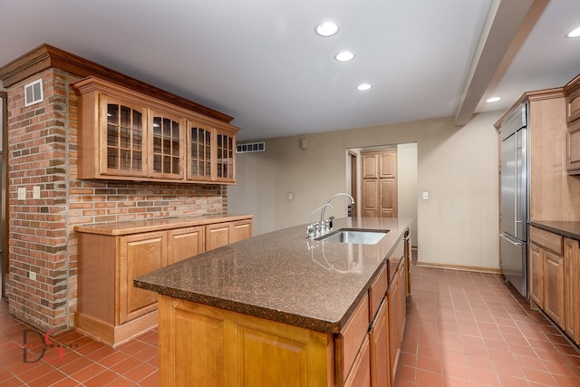 kitchen with a kitchen island with sink, sink, light tile patterned floors, beamed ceiling, and stainless steel built in refrigerator