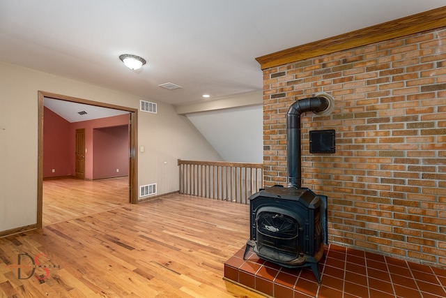 interior space featuring hardwood / wood-style flooring, a wood stove, brick wall, and vaulted ceiling