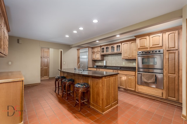 kitchen featuring decorative backsplash, light tile patterned floors, stainless steel appliances, and an island with sink