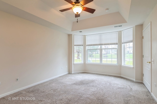 unfurnished room featuring a tray ceiling, light carpet, and ceiling fan