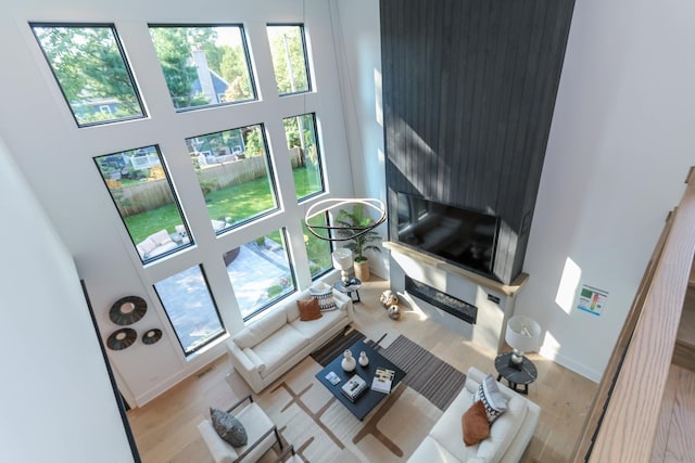 living room featuring a towering ceiling, plenty of natural light, light hardwood / wood-style floors, and a high end fireplace