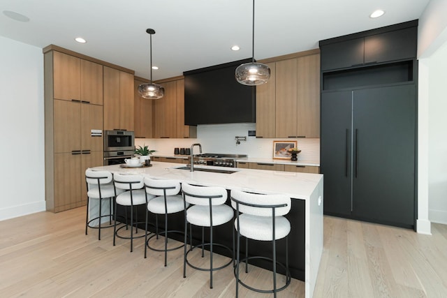 kitchen with hanging light fixtures, range hood, light hardwood / wood-style floors, and a center island with sink