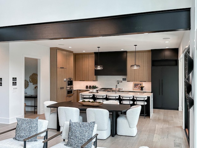 kitchen featuring tasteful backsplash, light hardwood / wood-style floors, hanging light fixtures, and a center island with sink