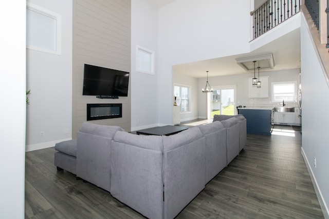 living room featuring a high ceiling, sink, dark hardwood / wood-style floors, a fireplace, and a notable chandelier