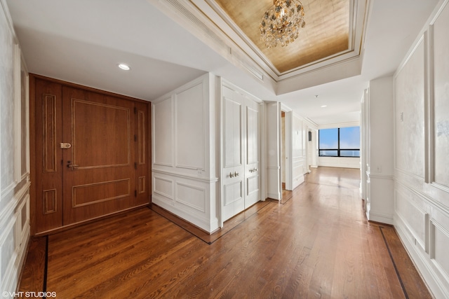 hall with a raised ceiling, crown molding, hardwood / wood-style floors, and an inviting chandelier