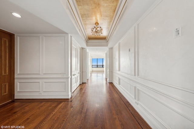 hallway featuring dark hardwood / wood-style floors, an inviting chandelier, crown molding, and a tray ceiling