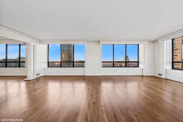 unfurnished living room featuring hardwood / wood-style flooring, a healthy amount of sunlight, crown molding, and decorative columns