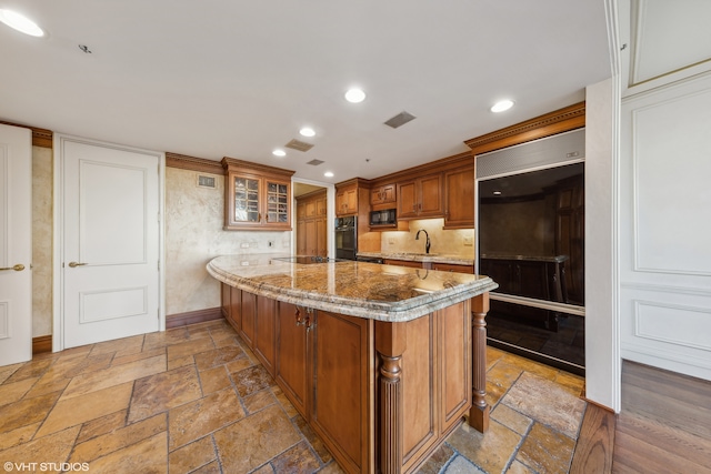 kitchen with kitchen peninsula, light stone counters, sink, and black appliances