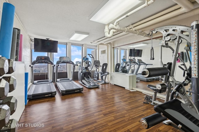 exercise room featuring a textured ceiling, dark wood-type flooring, and a wall of windows