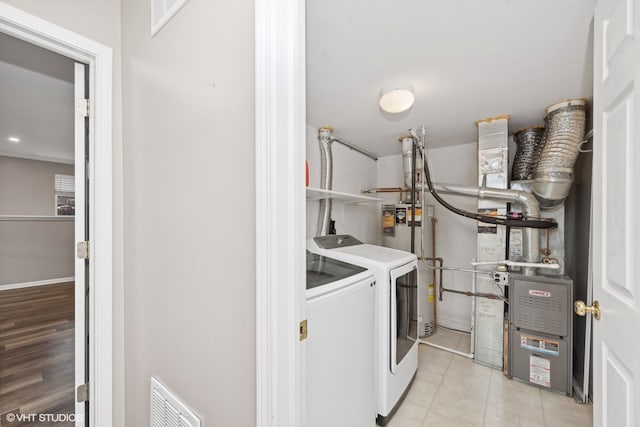 clothes washing area with washer and clothes dryer, heating unit, light wood-type flooring, and water heater