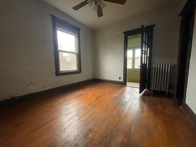 empty room with hardwood / wood-style floors, ceiling fan, and radiator heating unit