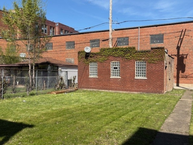 back of property featuring brick siding, fence, and a yard