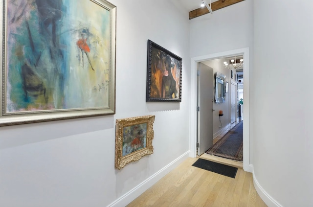 hallway with beamed ceiling, light wood-type flooring, and an inviting chandelier