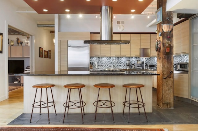 kitchen featuring a kitchen breakfast bar, built in fridge, hardwood / wood-style floors, and exhaust hood