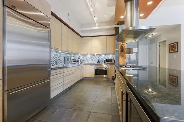 kitchen with dark stone counters, sink, appliances with stainless steel finishes, tasteful backsplash, and island range hood