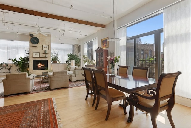 dining space featuring beamed ceiling, ceiling fan, light hardwood / wood-style floors, and a tiled fireplace