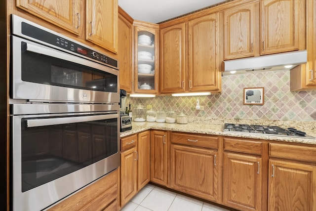 kitchen with appliances with stainless steel finishes, backsplash, light stone counters, and light tile patterned floors