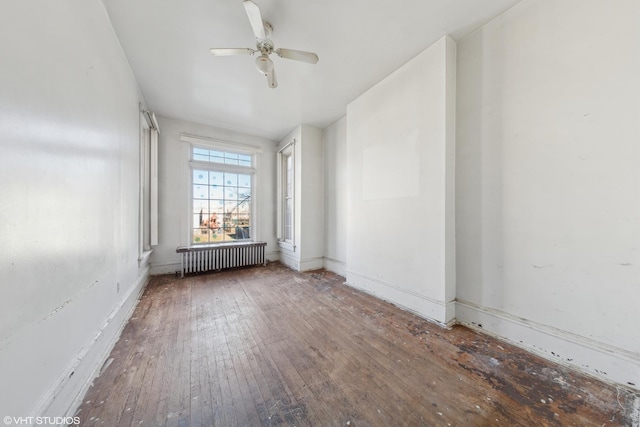 empty room featuring baseboards, radiator, hardwood / wood-style floors, and a ceiling fan