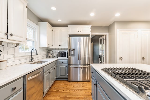 kitchen featuring sink, stainless steel appliances, backsplash, light hardwood / wood-style floors, and white cabinets