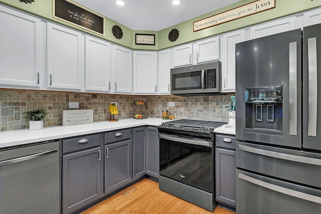 kitchen with light wood-type flooring, stainless steel appliances, gray cabinets, and backsplash