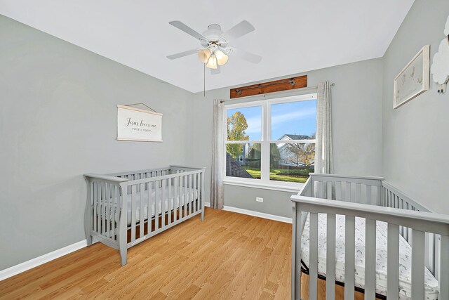 bedroom featuring hardwood / wood-style floors, ceiling fan, and a crib