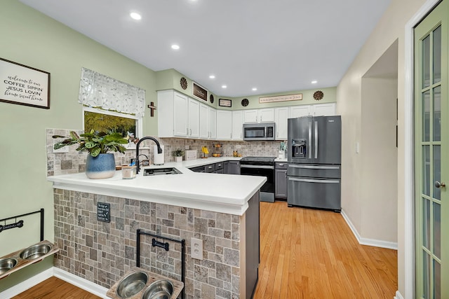 kitchen with sink, kitchen peninsula, appliances with stainless steel finishes, white cabinets, and light wood-type flooring