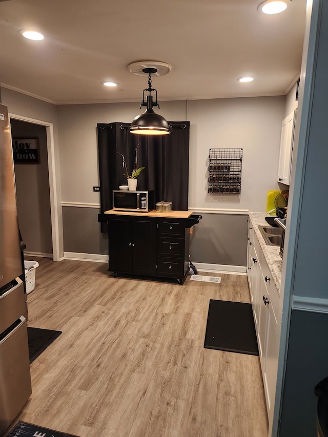 kitchen with stainless steel appliances, white cabinets, pendant lighting, and light wood-type flooring