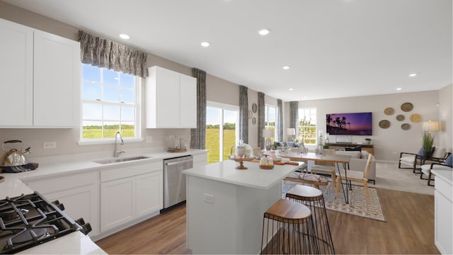 kitchen with white cabinets, hardwood / wood-style flooring, stainless steel dishwasher, and a kitchen island