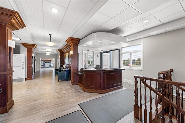 interior space featuring a paneled ceiling, light wood-type flooring, an island with sink, and ornate columns