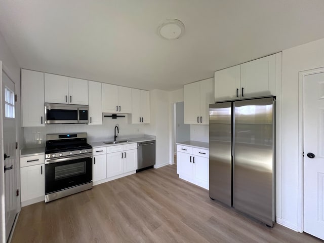 kitchen with stainless steel appliances, white cabinetry, and light hardwood / wood-style floors