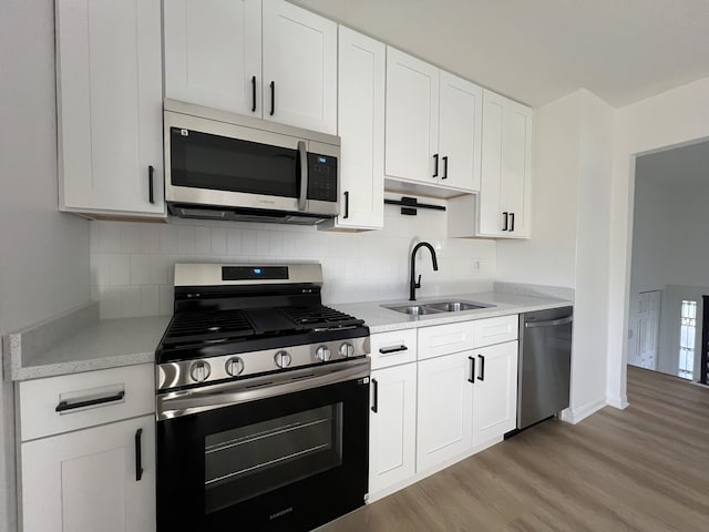 kitchen featuring backsplash, white cabinets, sink, appliances with stainless steel finishes, and light hardwood / wood-style floors