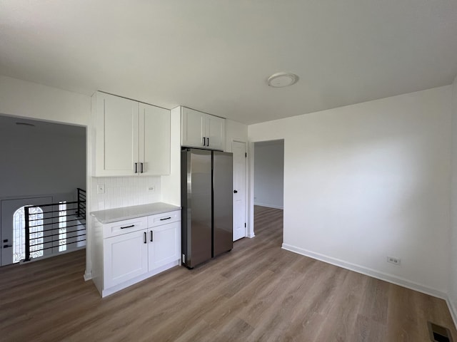 kitchen with white cabinets, backsplash, light hardwood / wood-style floors, and stainless steel refrigerator