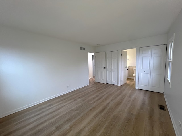 unfurnished bedroom featuring ensuite bathroom, light hardwood / wood-style floors, and two closets