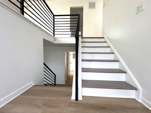 stairs featuring a towering ceiling and wood-type flooring