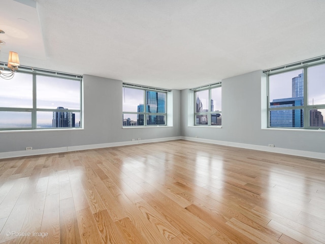 unfurnished room featuring light wood-type flooring, a wealth of natural light, and a chandelier