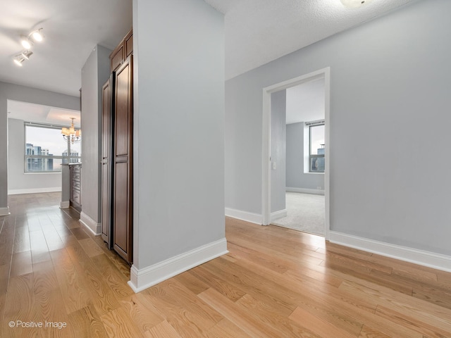 hallway featuring light wood-type flooring, a textured ceiling, and an inviting chandelier