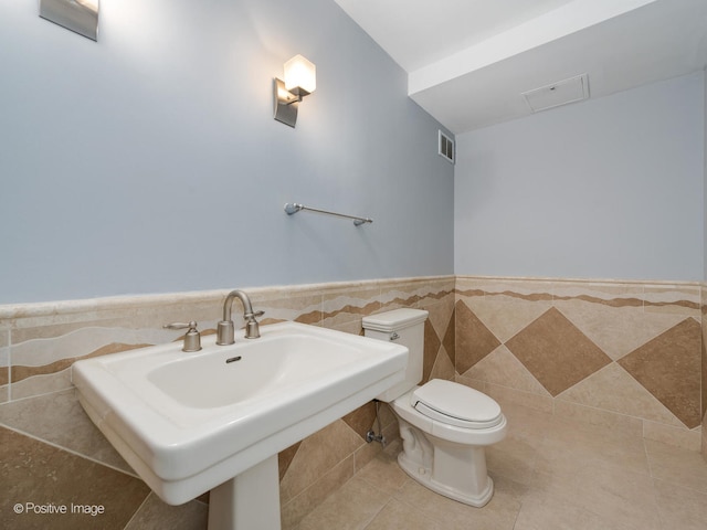 bathroom featuring tile patterned floors, toilet, tile walls, and sink