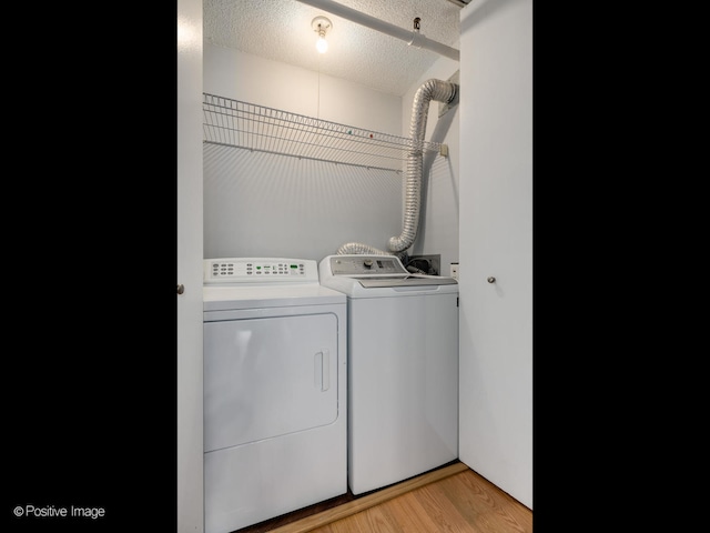 laundry room featuring washer and clothes dryer, light hardwood / wood-style flooring, and a textured ceiling