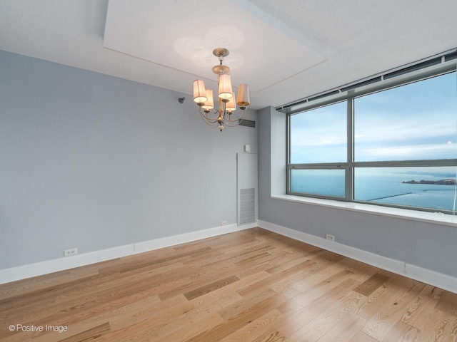 unfurnished room featuring a textured ceiling, light wood-type flooring, a water view, and an inviting chandelier