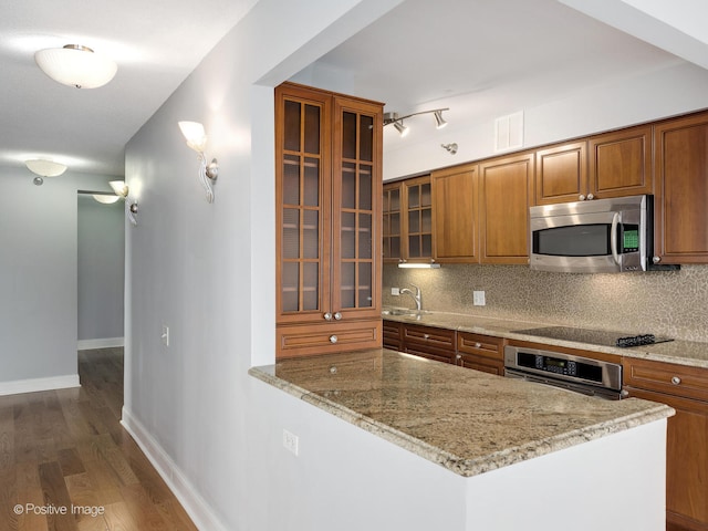 kitchen with decorative backsplash, appliances with stainless steel finishes, light stone counters, dark wood-type flooring, and sink