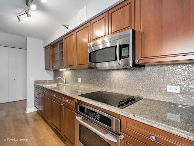 kitchen with tasteful backsplash, light stone counters, stainless steel appliances, sink, and light hardwood / wood-style flooring