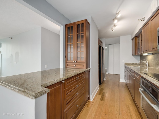 kitchen with black electric stovetop, oven, sink, light hardwood / wood-style flooring, and light stone countertops