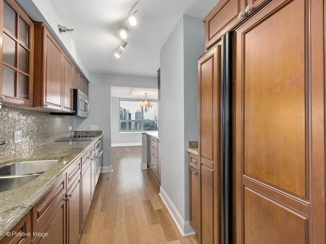 kitchen featuring light stone countertops, light wood-type flooring, tasteful backsplash, sink, and a notable chandelier