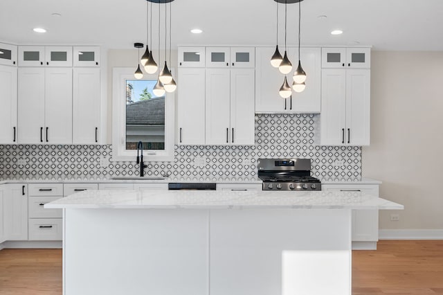 kitchen with light stone countertops, stainless steel gas range, white cabinets, light hardwood / wood-style floors, and a kitchen island